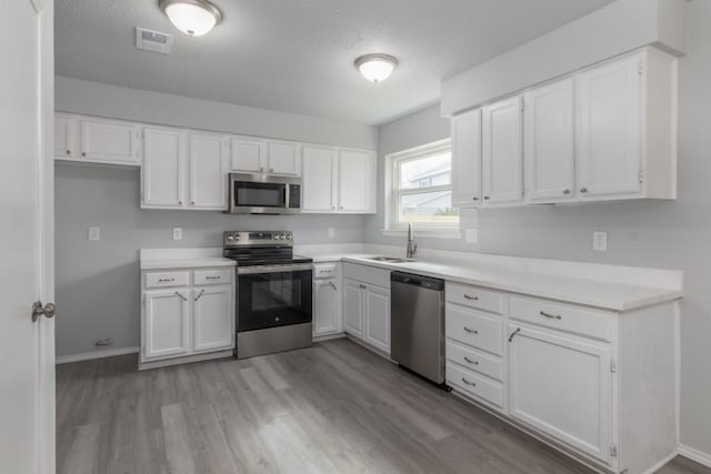 kitchen with white cabinets, appliances with stainless steel finishes, sink, and light hardwood / wood-style floors