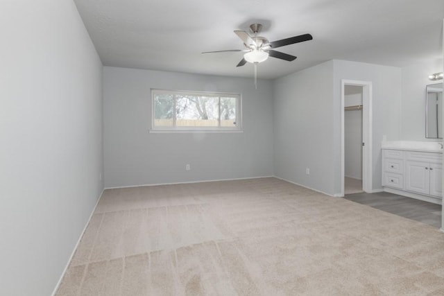 unfurnished bedroom with ceiling fan, connected bathroom, light carpet, and a walk in closet