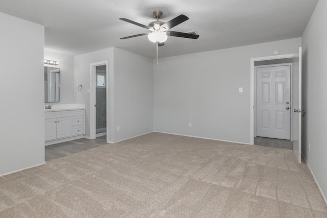 unfurnished bedroom featuring ensuite bath, light colored carpet, ceiling fan, and sink