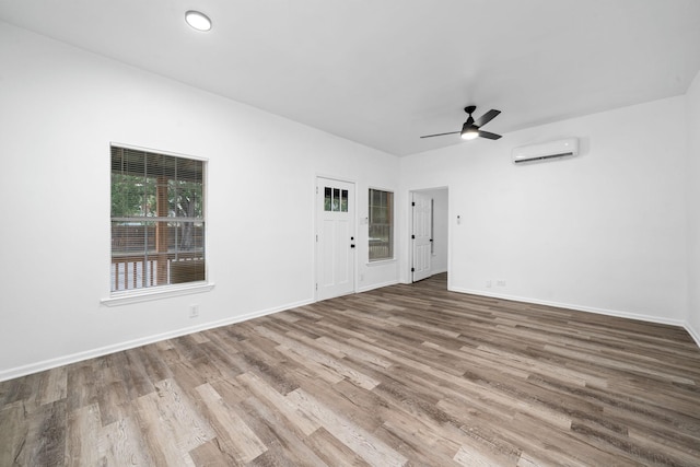 unfurnished room featuring ceiling fan, a wall mounted air conditioner, wood finished floors, and baseboards