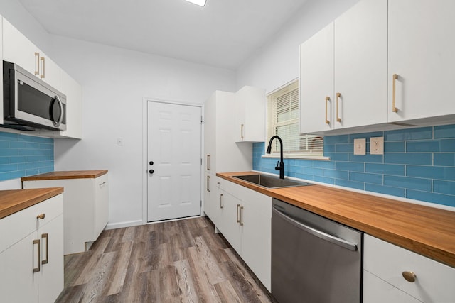 kitchen with sink, tasteful backsplash, wood-type flooring, white cabinets, and appliances with stainless steel finishes