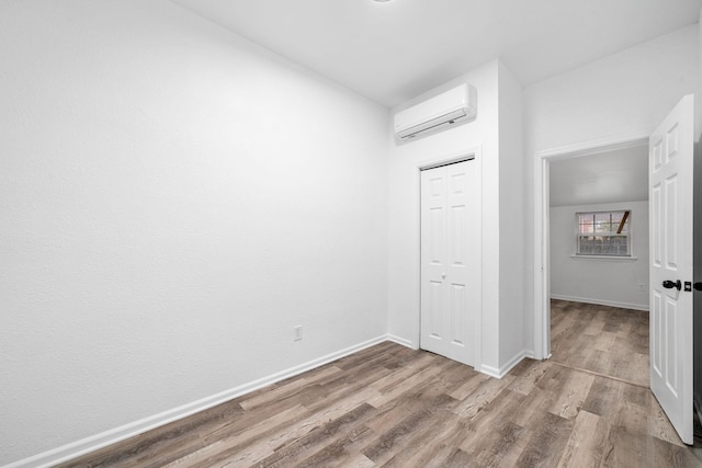 unfurnished bedroom with a closet, wood finished floors, baseboards, and a wall mounted AC