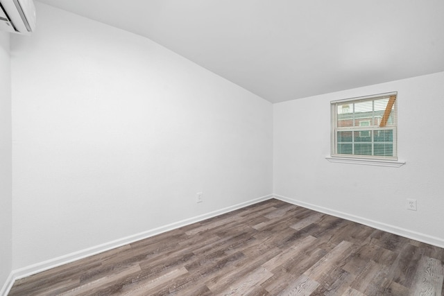 unfurnished room featuring lofted ceiling, baseboards, dark wood-style flooring, and a wall mounted air conditioner