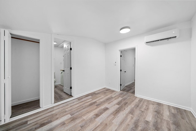 unfurnished bedroom featuring baseboards, an AC wall unit, and wood finished floors