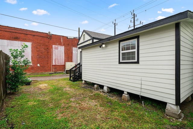 view of side of property with fence, a lawn, and roof with shingles