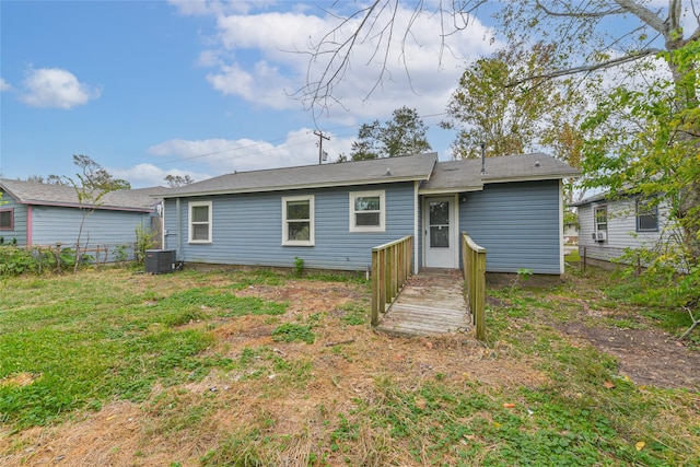 rear view of house with central AC unit and a yard