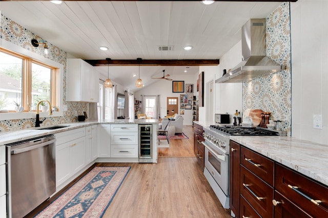 kitchen featuring appliances with stainless steel finishes, pendant lighting, wall chimney range hood, beverage cooler, and white cabinets