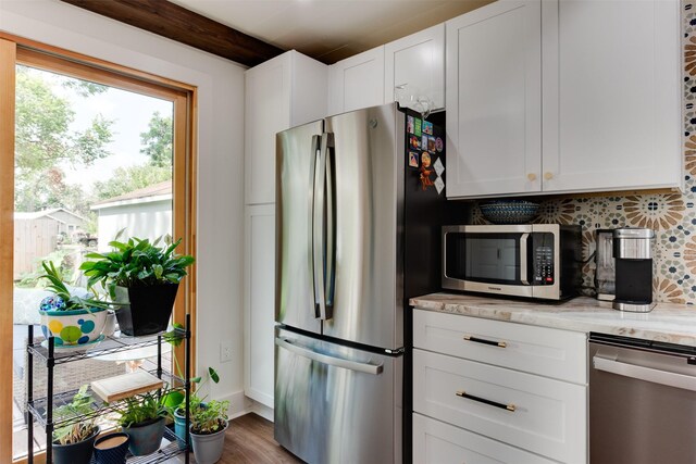 kitchen with tasteful backsplash, light stone counters, hardwood / wood-style floors, white cabinets, and appliances with stainless steel finishes