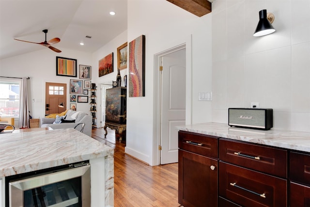 kitchen with ceiling fan, vaulted ceiling with beams, light stone counters, wine cooler, and light hardwood / wood-style floors