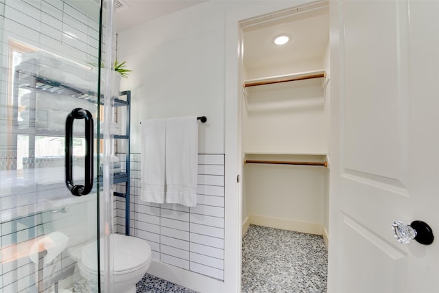 bathroom featuring toilet, walk in shower, and tile walls