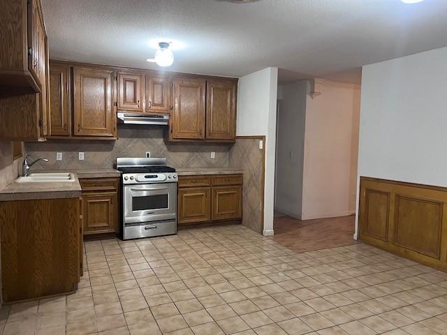 kitchen featuring backsplash, sink, light tile patterned flooring, and stainless steel range oven