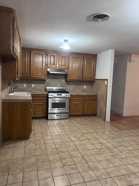 kitchen featuring a textured ceiling, sink, backsplash, and stainless steel range oven