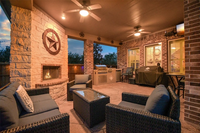 patio terrace at dusk featuring area for grilling, ceiling fan, an outdoor stone fireplace, and a grill