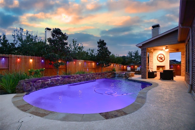 pool at dusk featuring ceiling fan, a patio, and an outdoor fireplace