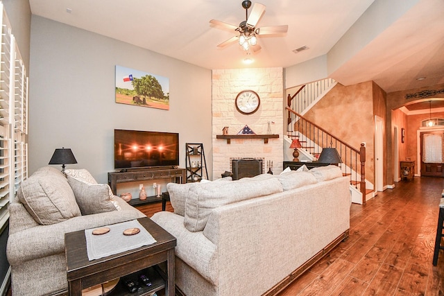 living room featuring wood-type flooring, a stone fireplace, and ceiling fan