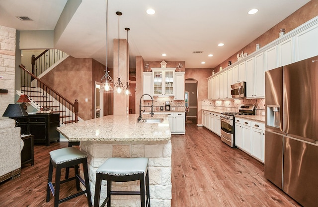 kitchen featuring light hardwood / wood-style flooring, pendant lighting, a breakfast bar area, a kitchen island with sink, and appliances with stainless steel finishes