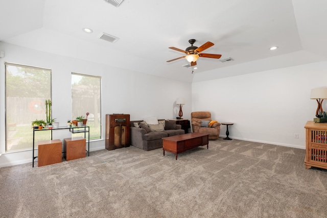 living room featuring a raised ceiling, ceiling fan, and light colored carpet