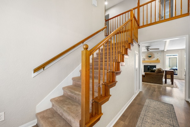 staircase with hardwood / wood-style floors, a large fireplace, ceiling fan, and beam ceiling