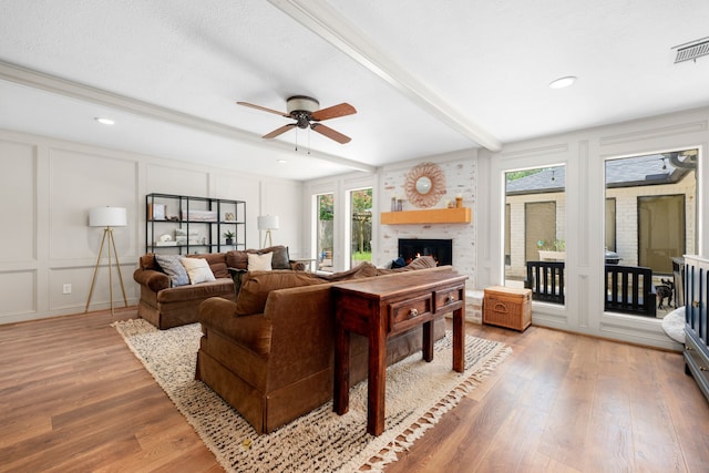 living room with ceiling fan, beamed ceiling, wood-type flooring, a textured ceiling, and a fireplace