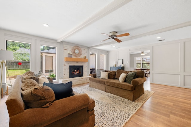 living room with a brick fireplace, light hardwood / wood-style flooring, a wealth of natural light, and beam ceiling