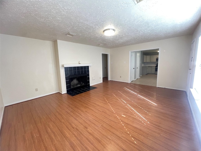 unfurnished living room with a tile fireplace, hardwood / wood-style floors, and a textured ceiling