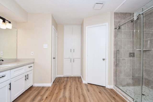 bathroom featuring hardwood / wood-style floors, vanity, a textured ceiling, and walk in shower