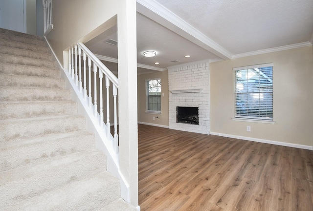 stairway featuring crown molding, plenty of natural light, wood-type flooring, and a brick fireplace