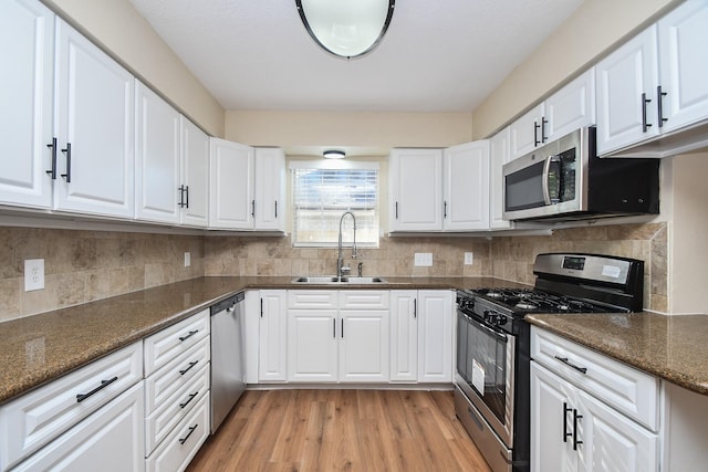 kitchen featuring white cabinetry, sink, light hardwood / wood-style floors, dark stone counters, and appliances with stainless steel finishes