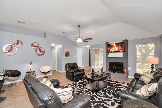 tiled living room featuring ceiling fan, vaulted ceiling, and a large fireplace