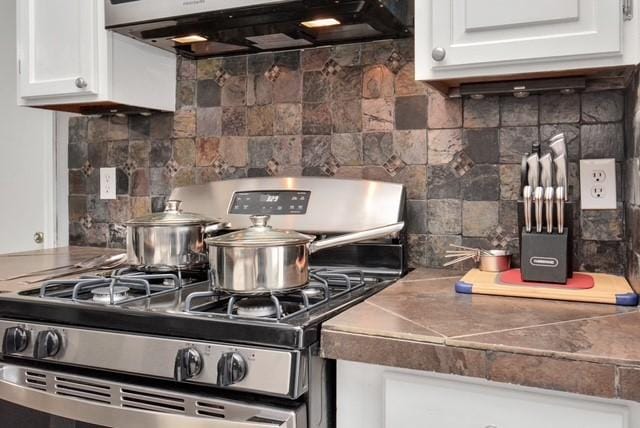 kitchen with decorative backsplash, stainless steel range with gas cooktop, white cabinetry, and range hood