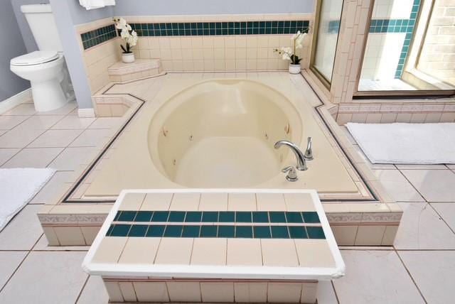 bathroom with a relaxing tiled tub, toilet, and tile patterned flooring