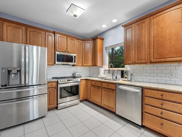 kitchen featuring appliances with stainless steel finishes, backsplash, light stone counters, sink, and light tile patterned floors