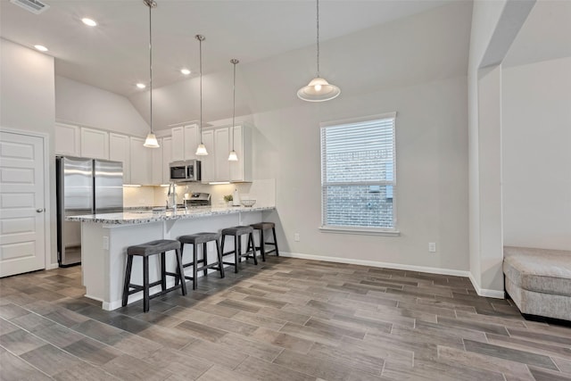 kitchen featuring kitchen peninsula, appliances with stainless steel finishes, decorative light fixtures, hardwood / wood-style floors, and white cabinetry