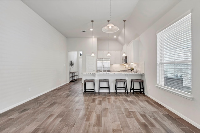 kitchen featuring lofted ceiling, decorative light fixtures, white cabinetry, kitchen peninsula, and stainless steel appliances