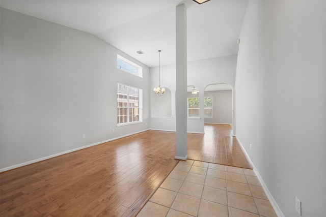 unfurnished living room with a chandelier, lofted ceiling, and light hardwood / wood-style flooring