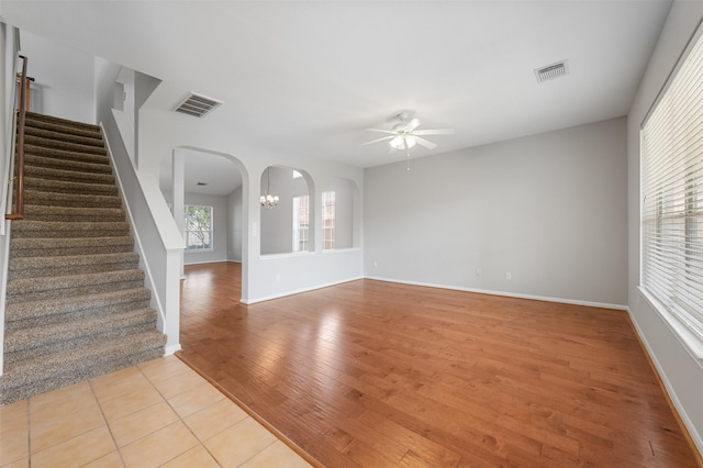 unfurnished living room featuring ceiling fan with notable chandelier and light wood-type flooring