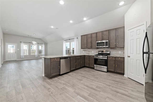 kitchen with decorative backsplash, appliances with stainless steel finishes, light wood-type flooring, light stone counters, and vaulted ceiling