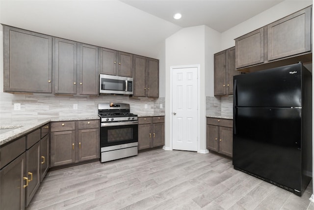 kitchen with lofted ceiling, backsplash, light hardwood / wood-style flooring, light stone counters, and stainless steel appliances