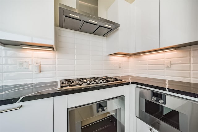 kitchen featuring stainless steel gas stovetop, oven, wall chimney range hood, tasteful backsplash, and white cabinetry