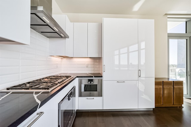 kitchen with white cabinetry, wall chimney exhaust hood, stainless steel appliances, dark hardwood / wood-style floors, and backsplash