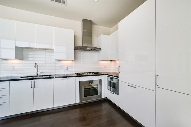 kitchen with stainless steel gas cooktop, sink, wall chimney range hood, white cabinetry, and oven