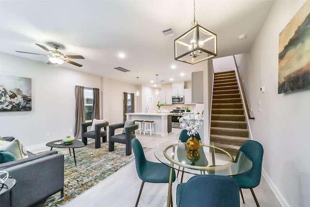 dining space with ceiling fan with notable chandelier and light wood-type flooring