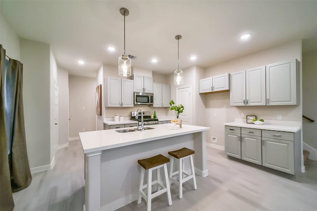 kitchen featuring appliances with stainless steel finishes, light wood-type flooring, a center island with sink, and hanging light fixtures