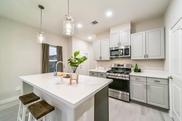 kitchen featuring sink, light hardwood / wood-style floors, decorative light fixtures, a center island with sink, and appliances with stainless steel finishes