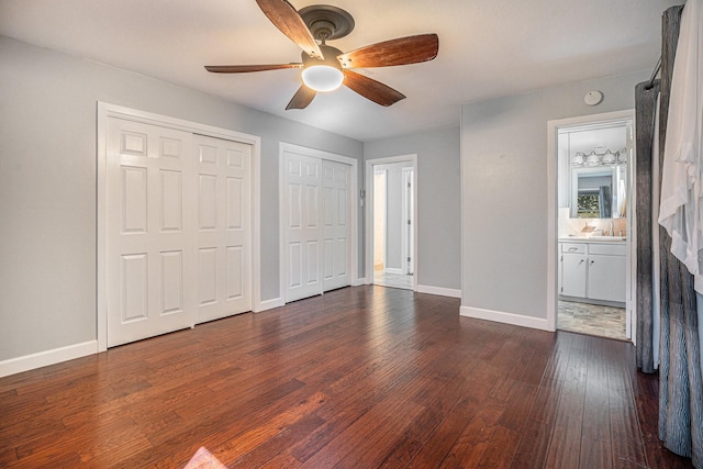 unfurnished bedroom featuring dark hardwood / wood-style flooring, ensuite bathroom, ceiling fan, sink, and multiple closets