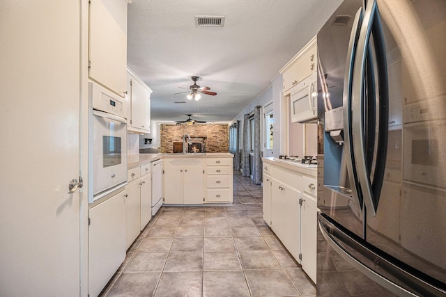 kitchen with white appliances, kitchen peninsula, ceiling fan, light tile patterned floors, and white cabinetry