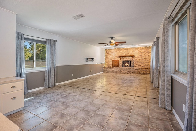 unfurnished living room featuring light tile patterned floors, a brick fireplace, ceiling fan, and brick wall