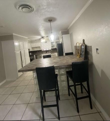 kitchen with kitchen peninsula, a kitchen breakfast bar, white cabinets, and ornamental molding