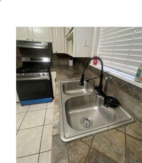 kitchen featuring white cabinets, light tile patterned floors, gas stove, and sink