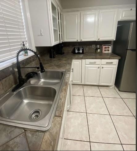 kitchen with white cabinets, light tile patterned floors, sink, and stainless steel refrigerator